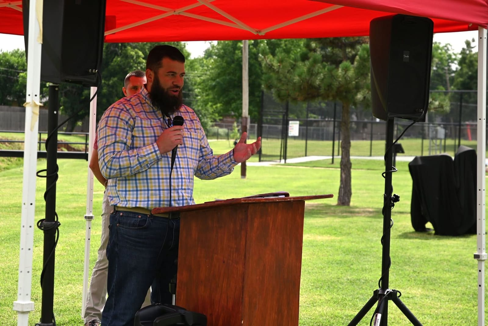 Mayor Brian Pillmore speaking at a microphone at an outdoor community event in a Yukon park