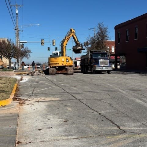 An excavator and dump truck working on South 5th Street in downtown Yukon, with the street’s brick buildings behind