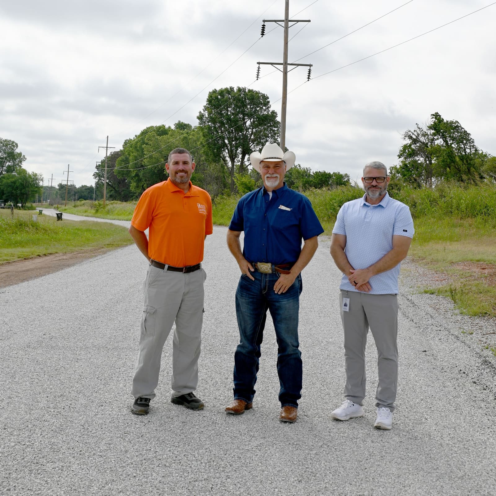 A City of Yukon public works officer and two other officials standing on a rural road surfaced with fresh chip-and-seal